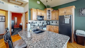 A kitchen with granite countertops, wooden cabinets, a black refrigerator, and a microwave. - Two BR condo w/ Brand NEW HOT TUB and great views! Community pool perfect for kids (Estes Park)