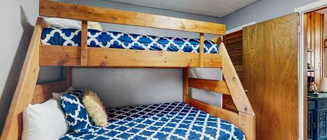 Un lit superposé avec une couvre-lit à motifs bleus et une tête de lit en bois.