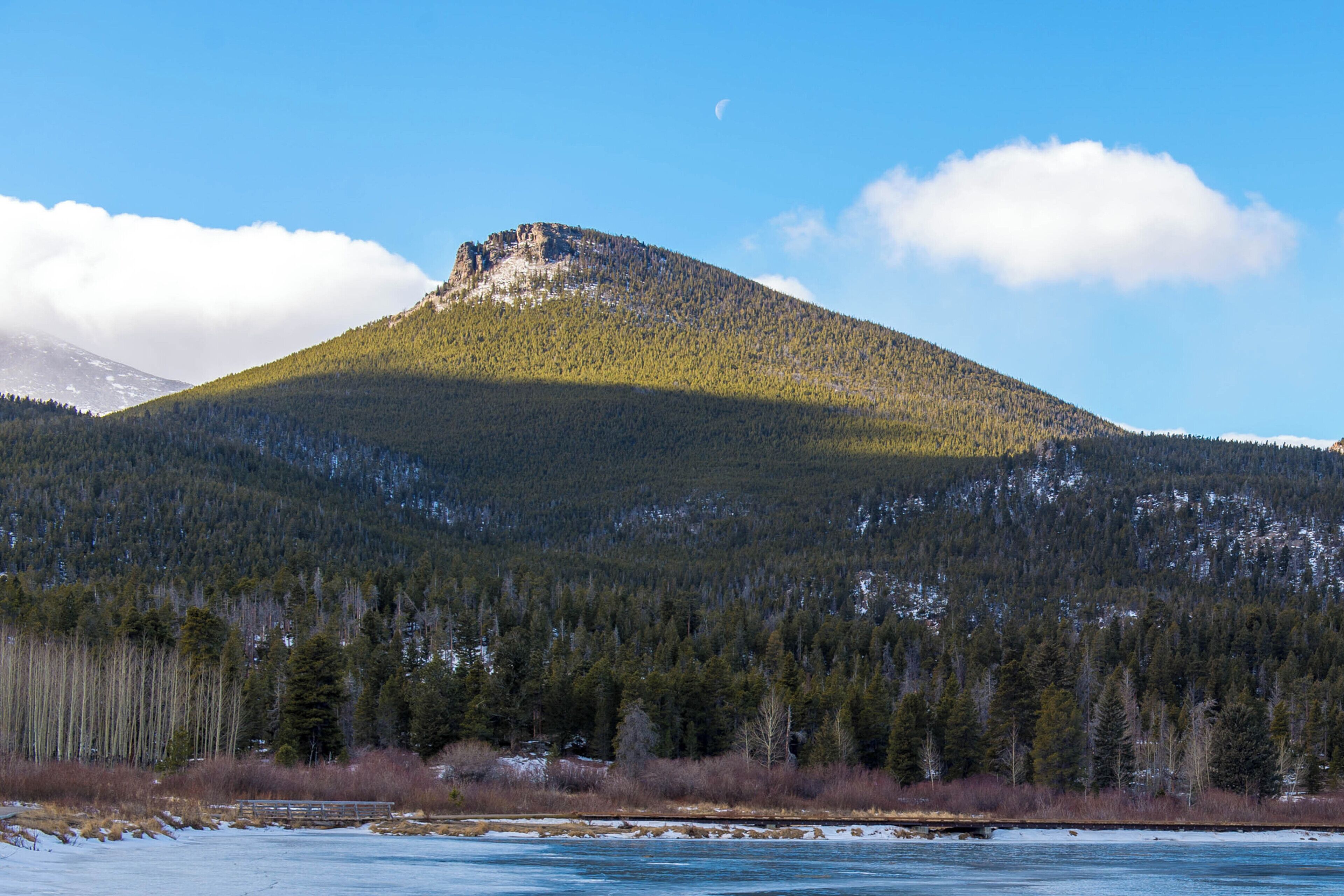 Ein Berg mit bewaldeter Flanke und blauem Himmel.