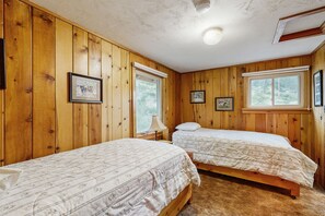 Une chambre avec deux lits, des murs en bois, des tableaux encadrés et des fenêtres.