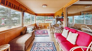 L’intérieur d’un chalet accueillant, avec un plafond en bois, de grandes fenêtres, un canapé rouge, un divan marron et un coin repas comprenant une table et des chaises.