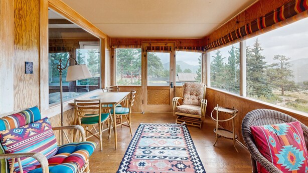 Une pièce chaleureuse avec un plafond en bois, de grandes fenêtres, un tapis à motifs et des meubles en osier.