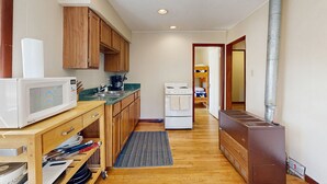 A compact kitchen with wooden cabinets, a microwave, a stove, and a wood-burning stove. - Ideal vacation home with wraparound deck & Rocky Mountain view (Estes Park)