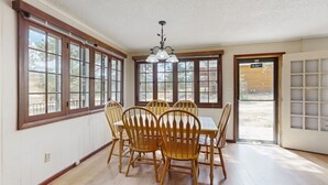 A dining area with a wooden table and chairs, large windows, and a ceiling light fixture. - Ideal vacation home with wraparound deck & Rocky Mountain view (Estes Park)