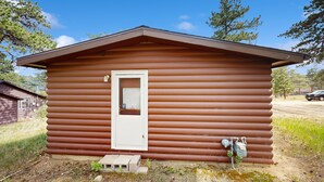 A small, single-story log cabin with a white door and a small window. - Ideal vacation home with wraparound deck & Rocky Mountain view (Estes Park)