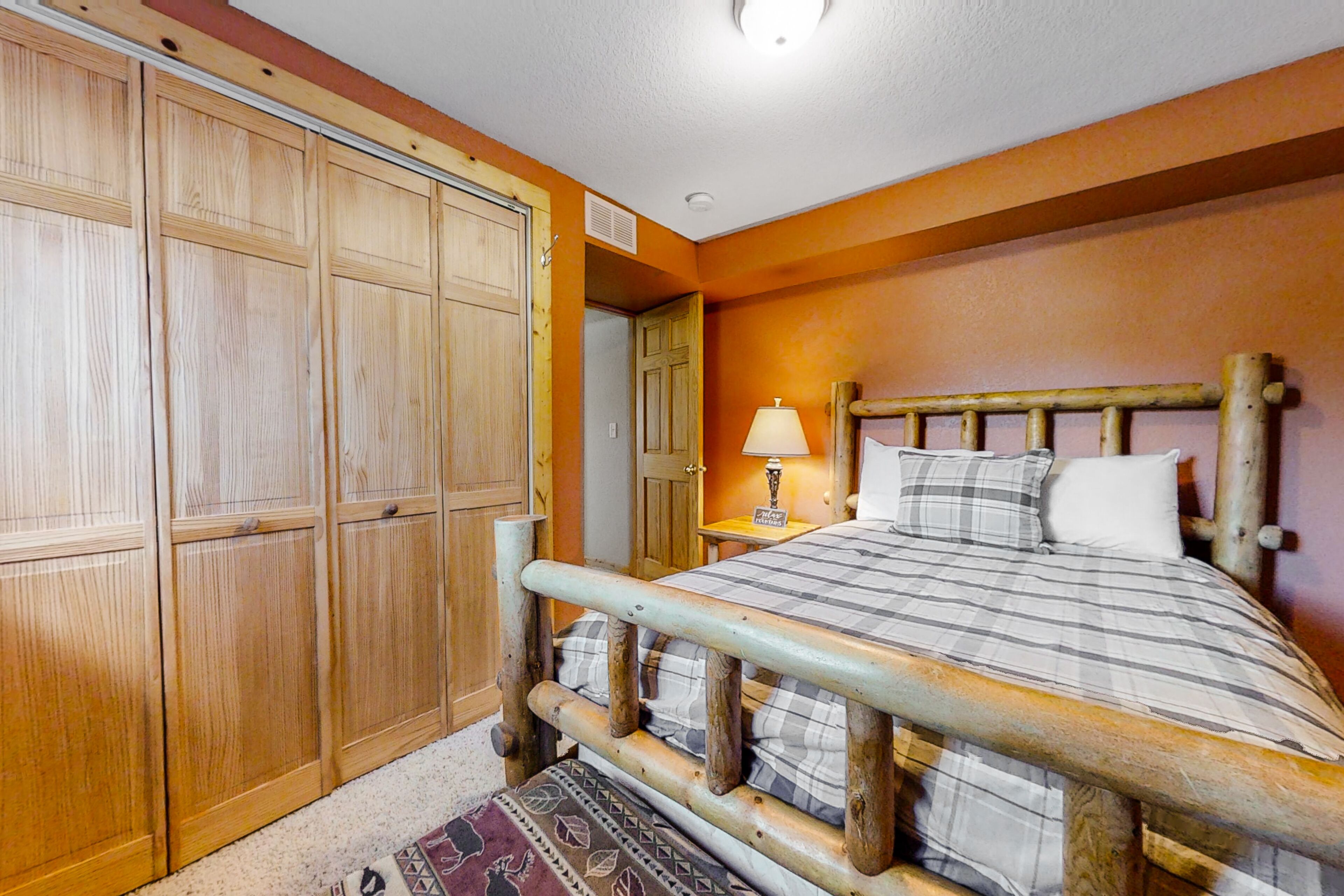 A bedroom with a wooden bed frame, a wardrobe, and a bedside table with a lamp.