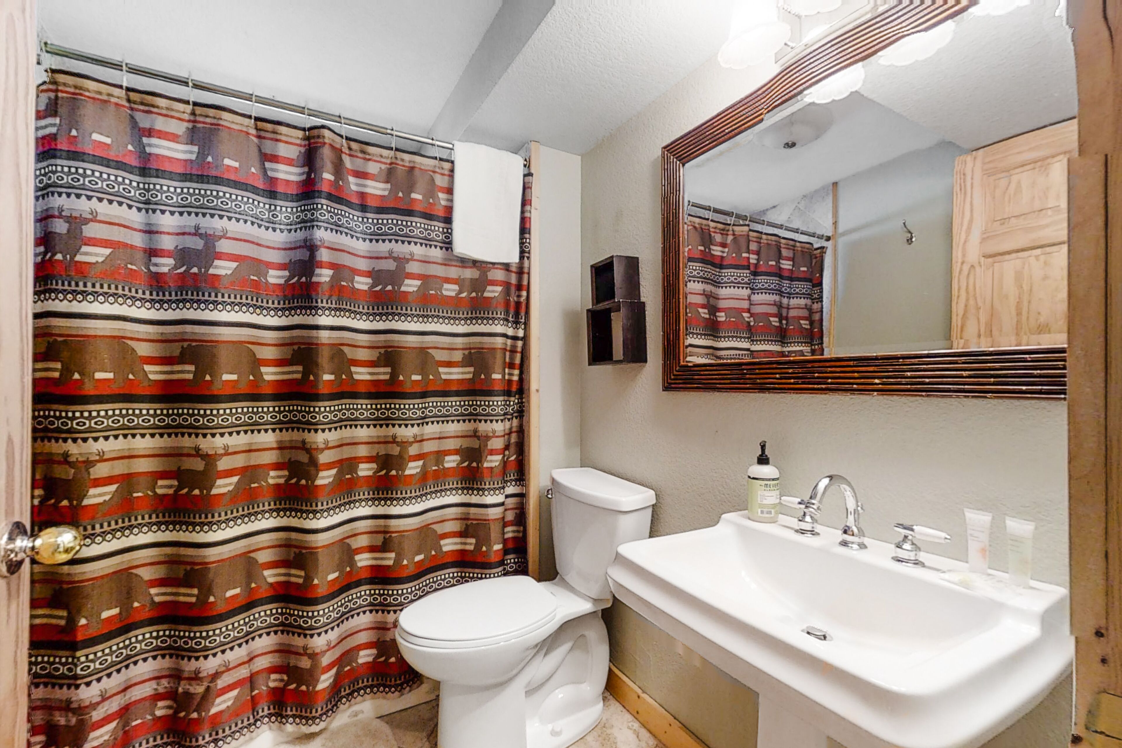 Une salle de bain avec un rideau de douche à motifs, des toilettes, un lavabo avec des articles de toilette et un miroir.