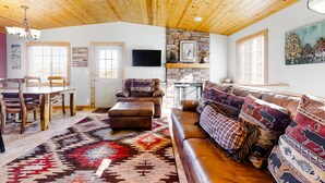 A cozy living room with a wooden ceiling, a stone fireplace, a leather sofa, and a dining area with a wooden table and chairs. - Wonderful family cabin w/stunning views, free WiFi, & full kitchen - near trails (Estes Park)