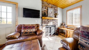 A living room with a stone fireplace, leather sofas, a wooden ceiling, and a TV mounted on the wall. - Wonderful family cabin w/stunning views, free WiFi, & full kitchen - near trails (Estes Park)