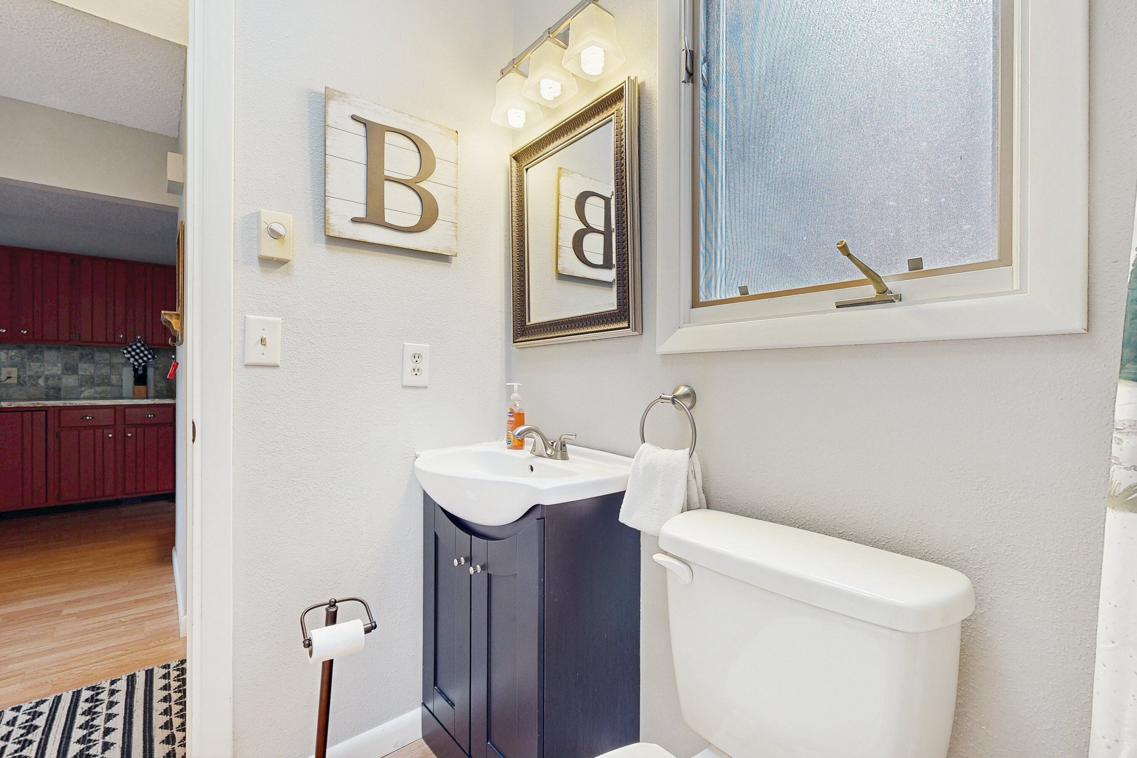 A bathroom with a toilet, sink, and mirror. There are wooden cabinets and a rug on the floor.