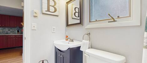 A bathroom with a toilet, sink, and mirror. There are wooden cabinets and a rug on the floor.
