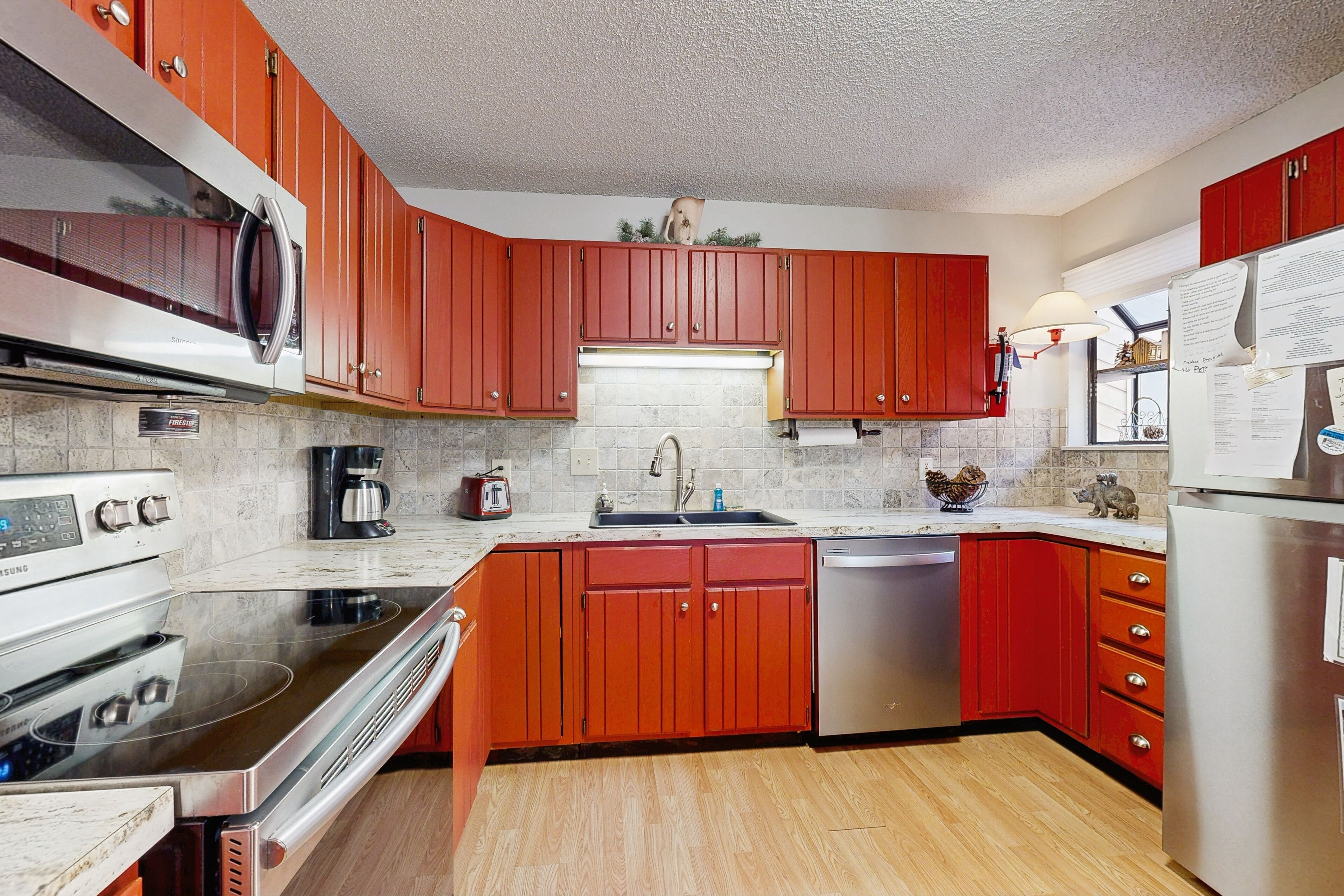Una cocina con armarios rojos, electrodomésticos de acero inoxidable, un lavamanos y un refrigerador.