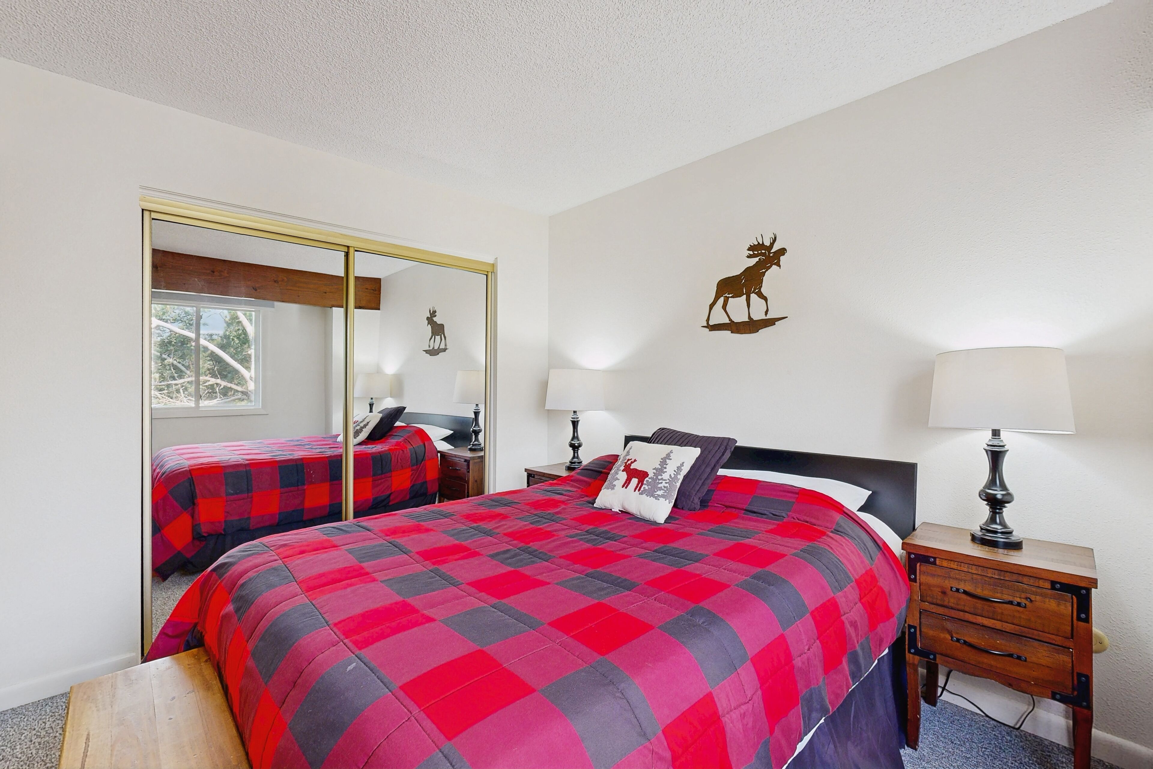 A bedroom with two beds, a mirror, a nightstand, and a wall-mounted lamp.
