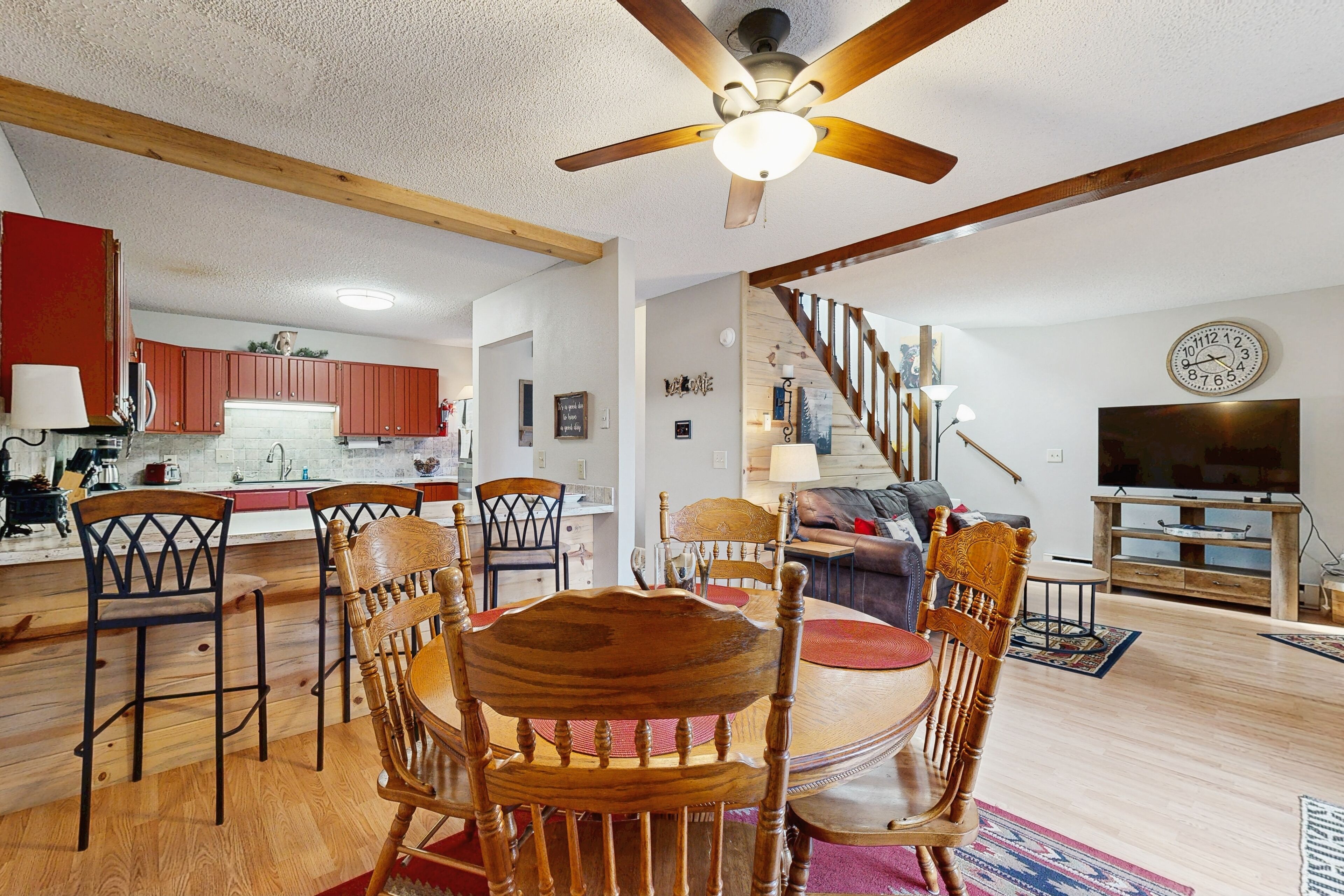 A spacious living area with a dining table surrounded by wooden chairs, a ceiling fan, and a staircase leading to an upper level.