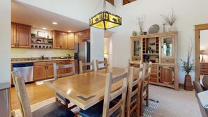A spacious kitchen with wooden cabinets, a large dining table, and a hanging light fixture. - Modern home with full kitchen, patio, great location-Dogs Welcome (Estes Park)