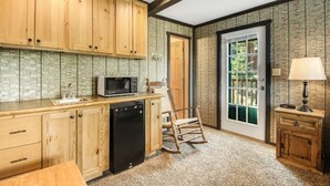 Una cocina con armarios de madera, microondas, lavavajillas, una mecedora y una puerta que da al exterior.