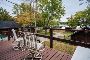 A wooden deck with two rocking chairs, a view of a lake, and a wooden cabin in the background. - Hilltop Haven at Sommer Dorf (West Branch)