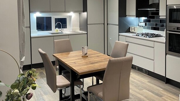 Une cuisine moderne avec un coin repas, comprenant une table en bois, des chaises et une vue sur la cuisine grâce à une cloison en verre.