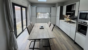 Une cuisine moderne dotée d’une verrière, de meubles blancs et d’un coin repas avec une table et des chaises en bois.