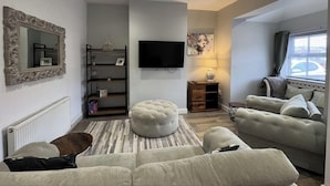 Un salon comprenant un canapé, un pouf, une télévision et une cheminée.