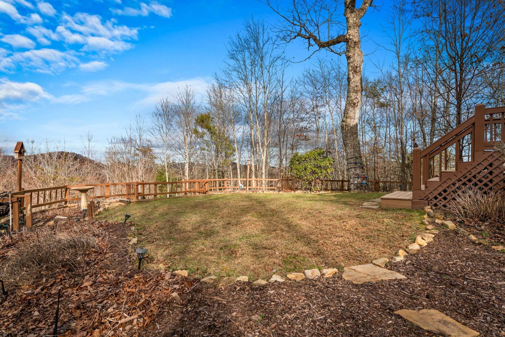 A backyard with a wooden deck, stone pathway, and a fenced area.