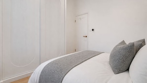 Un dormitorio con cama, almohadas grises, una puerta blanca y una lámpara.