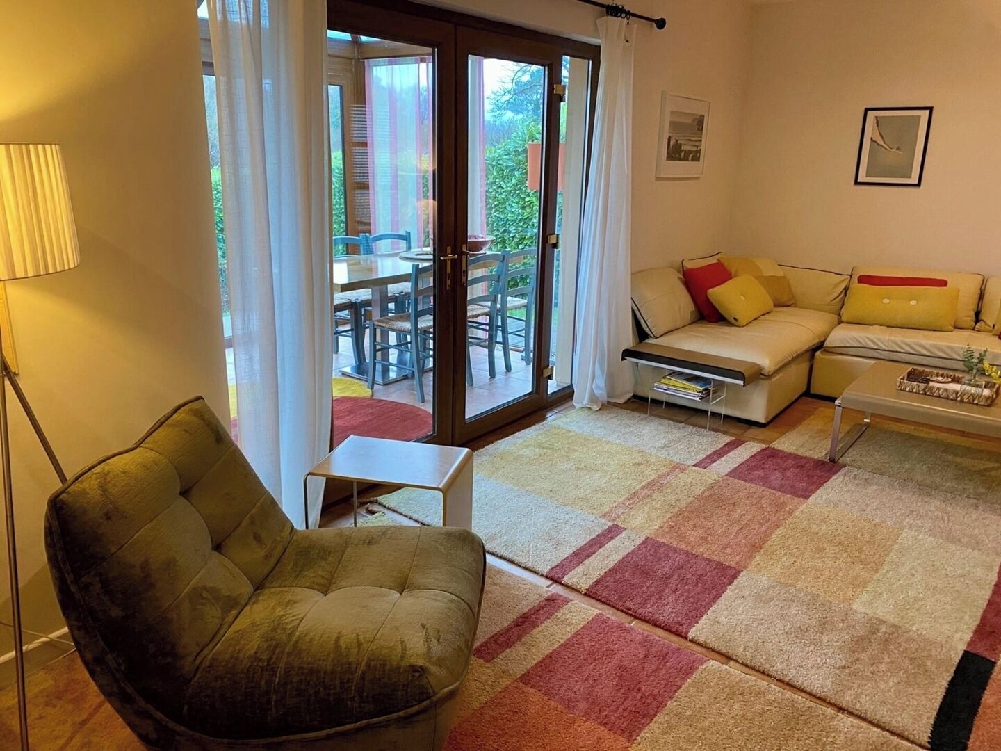 A living room with a sofa, a small table, a chair, and a view through a glass door to an outdoor dining area.