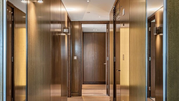 Un couloir doté de portes en bois et d’un plancher ciré, qui mène à une pièce avec un grand miroir et une porte.