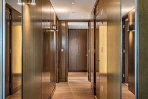 Un couloir doté de portes en bois et d’un plancher ciré, qui mène à une pièce avec un grand miroir et une porte.
