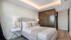 Une chambre d’hôtel moderne avec un grand lit, des lampes de chevet, une armoire en bois et un luminaire au plafond.