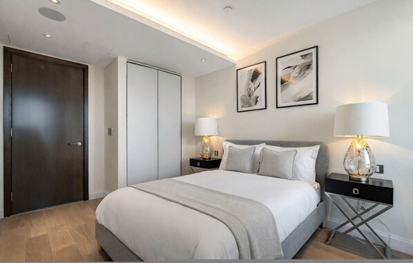 A modern bedroom with a large bed, two bedside tables with lamps, a wardrobe, and abstract art on the wall. - Ultra Modern Home - Amazing Views Gym Spa (London)