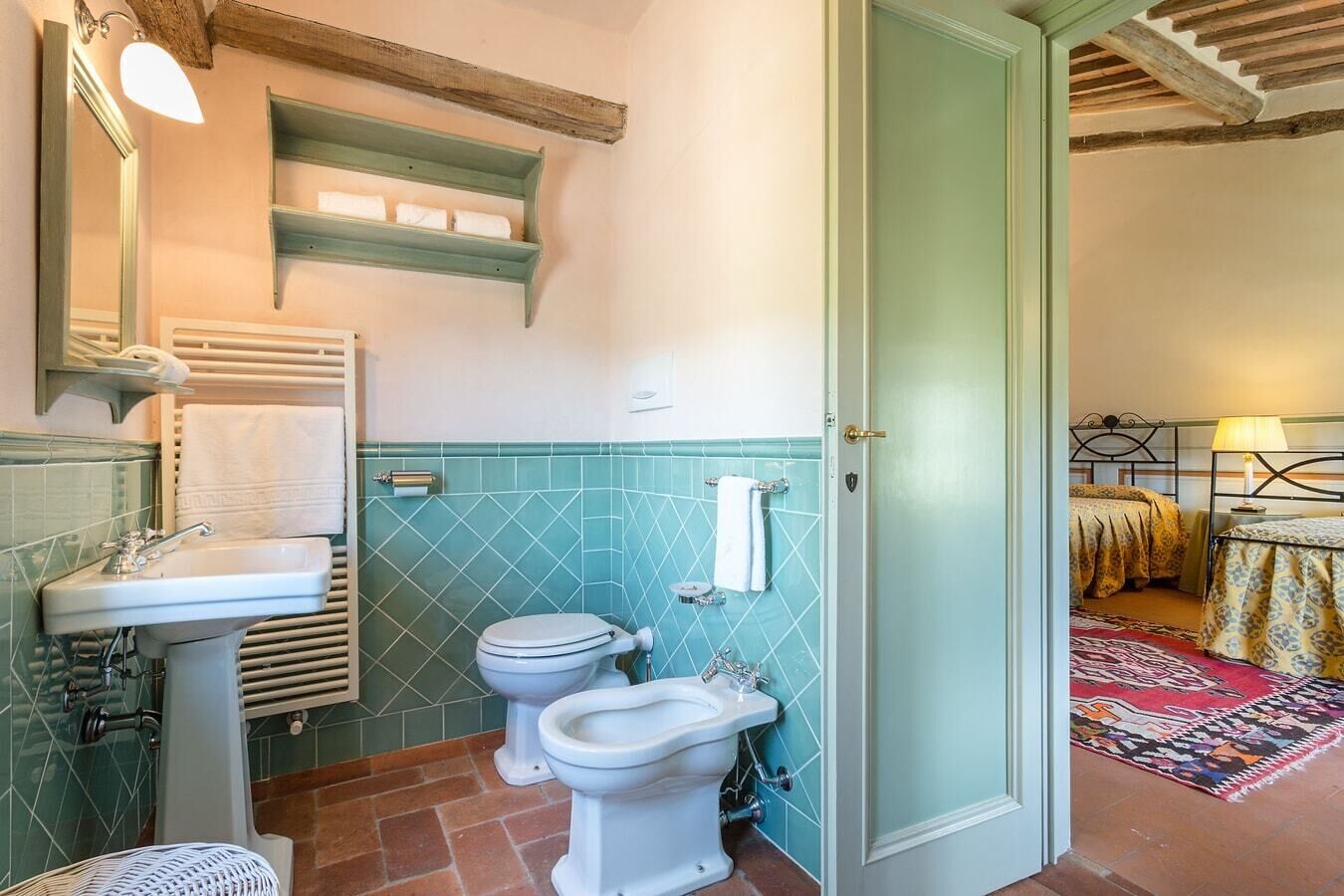 A bathroom with a sink, two toilets, a towel rack, and a shower area.