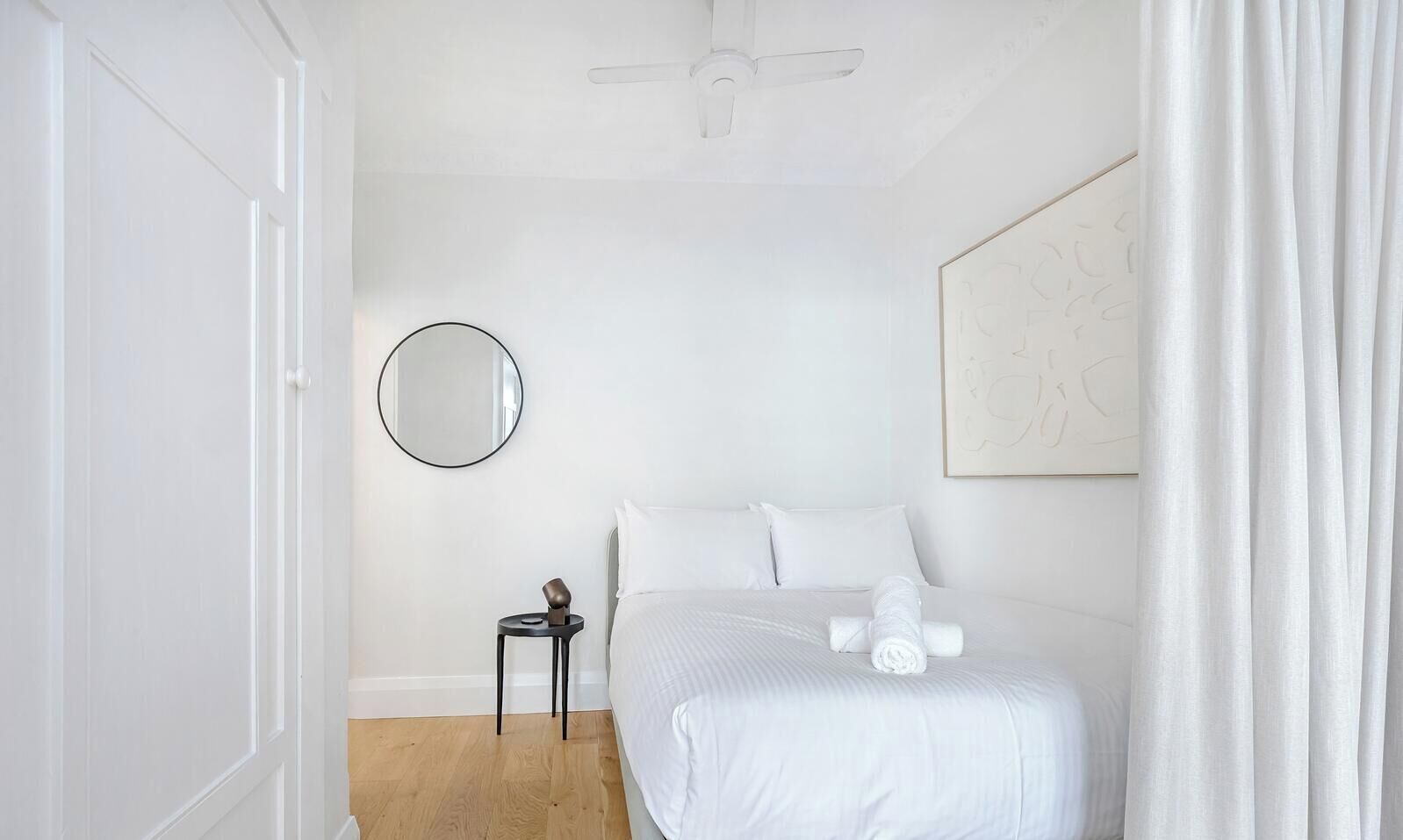 Une chambre à coucher avec un lit, un miroir rond, une petite table et un ventilateur de plafond.