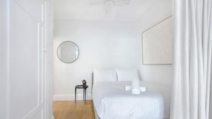 A bedroom with a bed, a round mirror, a small table, and a ceiling fan.
