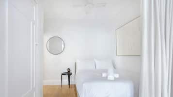 Une chambre à coucher avec un lit, un miroir rond, une petite table et un ventilateur de plafond.