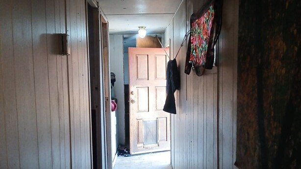 Un pasillo estrecho con paredes de madera y suelo de baldosas. Al final del pasillo, hay una puerta y un perchero con una chaqueta.