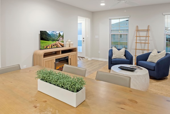 A modern living room with a wooden dining table, a blue sofa, and a television on a wooden stand.