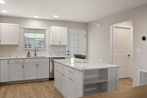 A modern kitchen with white cabinetry, a marble island, and a built-in sink.
