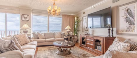 A spacious living room with a sofa set, a coffee table, a TV, and a large window with a view.