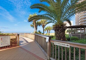 A wooden walkway leading to a beach with palm trees and a sign indicating restrooms. - Hidden Luxury 703-Gulf-Front Luxury-Sleeps 10 (Panama City)