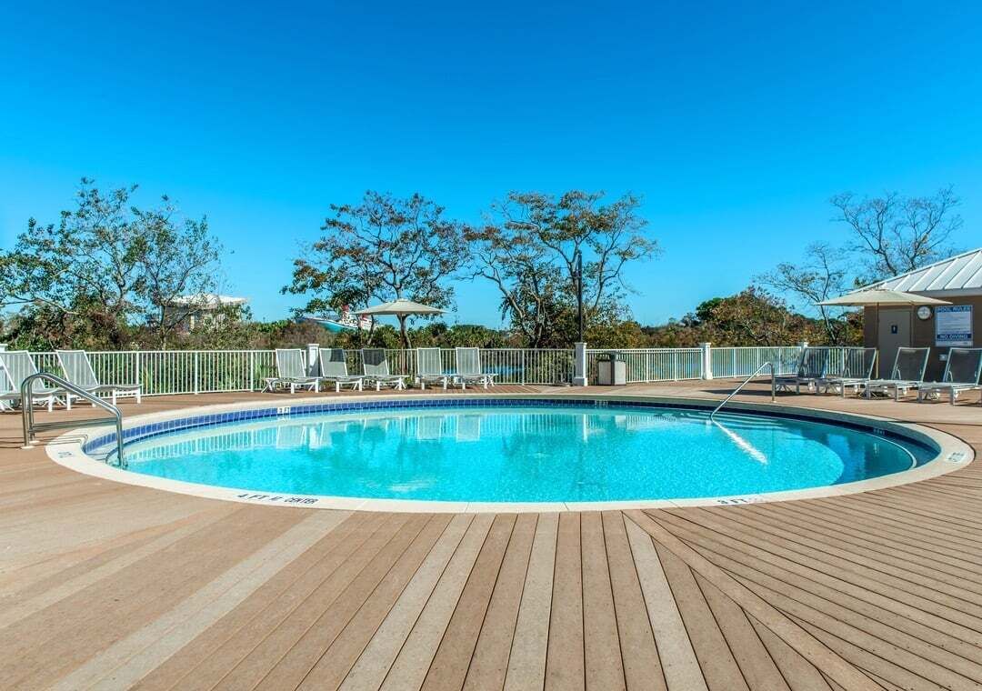 A pool area with a wooden deck, lounge chairs, and a fenced swimming pool.
