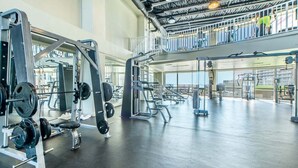 A spacious gym with various weightlifting equipment, a mezzanine level, and large windows. - Deja Blue 1831–Pools & Beach–Sleeps 8 (Panama City)