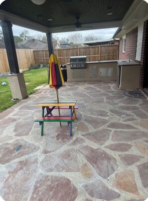 An outdoor patio with a stone floor, a barbecue grill, and a colorful table.