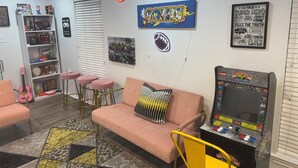 A room with a pink sofa, a gaming console, a guitar, and various board games. - Luxurious, peaceful, & fun 4-bedroom house with a game room in charming La Porte (La Porte)