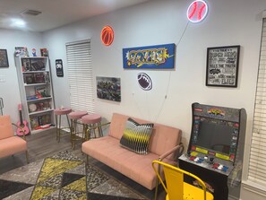 A room with a pink sofa, a gaming console, a guitar, and various board games. - Luxurious, peaceful, & fun 4-bedroom house with a game room in charming La Porte (La Porte)