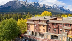 A hotel with a stone facade, multiple stories, and a balcony. It is located in a mountainous area with a view of snow-capped peaks. - Rustic Creekside Retreat 2BR and 2BT with Stunning View! (Canmore)