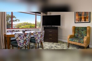 Une pièce comprenant une table à manger, des chaises, un téléviseur, un meuble et une fenêtre donnant sur un beau paysage.