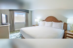 Une chambre d’hôtel avec un grand lit, un téléviseur posé sur une commode et une fenêtre avec des rideaux.