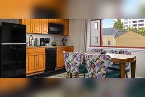 Une cuisine compacte avec des meubles de rangement en bois, un réfrigérateur noir et un four à micro-ondes. On y trouve également un coin repas avec une table et des chaises à motifs.