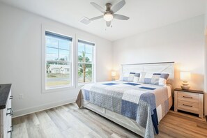 A bedroom with a bed, two bedside lamps, a ceiling fan, and large windows. - Pool | Walk to Beach | Oleander Breeze | Golf Cart | Panama City Beach (Panama City Beach)